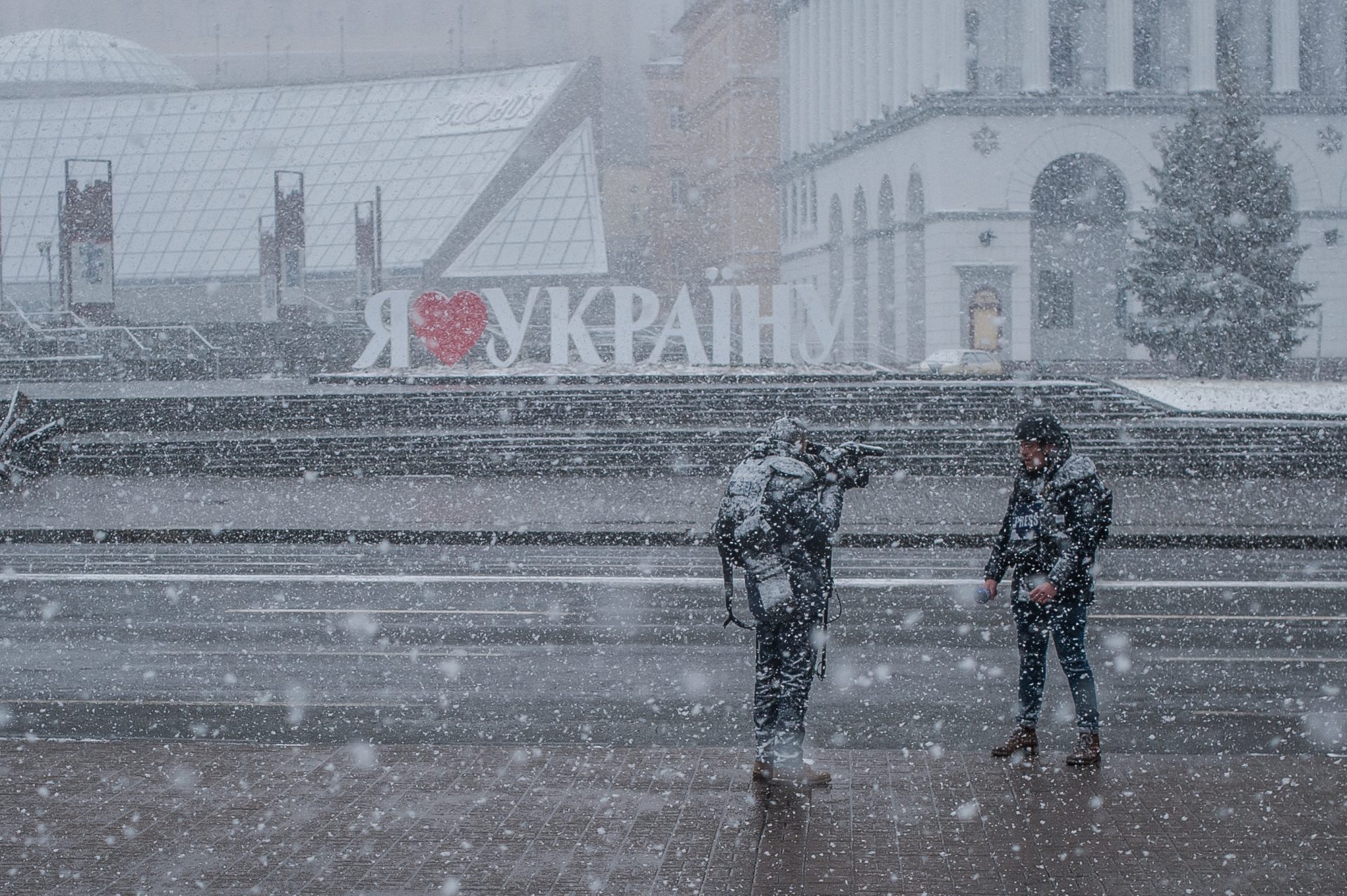 Two reporters standing in front of a "I Love Ukraine" sign