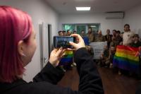 A woman with pink hair taking a picture of a group of military personnel holding LGBTQ+ flags